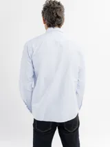 Camisa de manga larga con diseño de rayas finas, cuello con botones y bolsillo frontal. Presenta cierre de botonadura frontal y corte regular.