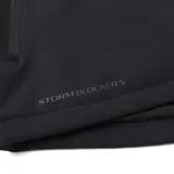 Chaqueta negra con capucha extraíble y ajustable, confeccionada con tecnología Storm Blocker+ para protección contra agua y viento. Cuenta con cierre frontal completo, bolsillos laterales y en el pecho con cremalleras impermeables, y logo de la marca en contraste amarillo.