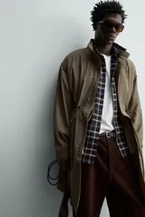 Parka relaxed fit de tejido técnico ligero, color verde militar, con cuello subido, manga larga y bolsillos de plastrón con solapa en la cadera. Cuenta con cintura ajustable con cordones y cierre frontal con cremallera oculta por solapa con botones a presión.