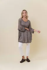 Buzo de tejido liviano y calado con brillo sutil, color gris oscuro o negro. Presenta un calce amplio y mangas amplias, con un detalle de tiras entrelazadas en la espalda. El largo es irregular, más largo en la parte trasera.