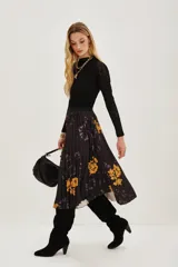 Falda midi plisada de color negro con estampado floral en tonos amarillos y detalles de efecto tie-dye. Presenta una silueta acampanada con movimiento y cintura elástica.