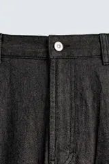 Pantalón de jeans de algodón ligero, color negro lavado, con corte balloon fit (holgado y ancho). Presenta pliegues frontales marcados en la cintura y cierre frontal de cremallera y botón.