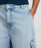 Bermuda cargo de corte baggy confeccionada en denim de algodón. Presenta cintura con trabillas, cierre frontal con botón y cremallera, y bolsillos laterales utilitarios de gran tamaño.