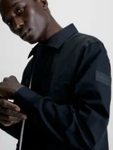 Camisa negra de popelina con corte relaxed, cierre frontal con botones, mangas largas y dos bolsillos con solapa en el pecho.