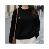 Buzo negro de punto con diseño trenzado y cuello redondo, de manga larga y ajuste cómodo con puños y dobladillo acanalados. Presenta una pequeña etiqueta metálica decorativa en el pecho.