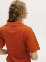 Chomba de punto negro, de manga corta, con cuello tipo polo, escote en V abotonado con detalles de crochet en los bordes y terminaciones acanaladas.