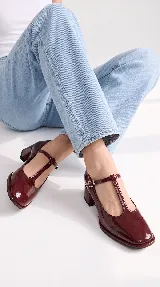 Zapatos de tacón bajo tipo Mary Jane con tira en T, confeccionados en charol color burdeos, con puntera cuadrada y cierre de hebilla lateral.