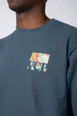 Remera de corte oversize color beige, confeccionada en algodón grueso. Presenta una estampa frontal pequeña con diseño artístico abstracto en tonos azules y amarillos.