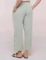 Pantalón de algodón rústico color verde, de tiro medio-alto con pretina elastizada y bolsillos laterales. Presenta corte holgado, diseño cropped de pierna ancha y aberturas laterales en los tobillos con detalles de botones.