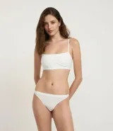 Soutien tipo top, color blanco, confeccionado en tejido seamless de poliamida y elastano. Presenta tirantes finos ajustables y un ribete contorneado bajo el busto.