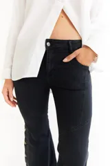 Jean de corte oxford con tiro medio, confeccionado en denim negro. Presenta recortes curvos en las piernas y detalle de botones metálicos en los laterales de la botamanga.