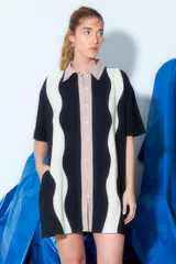 Túnica corta con cuello camisero y cierre frontal con botones. Diseño con bloques de color negro, beige y blanco con patrón de zig zag.