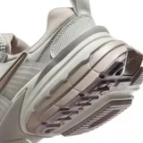 Championes Nike V2K Run de estilo retro-futurista, con diseño en capas de malla y material sintético en tonos beige y gris. Presenta una entresuela robusta con tecnología Cushlon y el logo de Nike en el lateral.