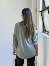 Remera de manga larga color verde, con cuello redondo y diseño holgado. Presenta un detalle frontal con parches de lentejuelas plateadas y estampado tipográfico.