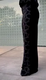 Pantalón de corte recto y tiro alto, confeccionado en terciopelo negro con un diseño calado geométrico que revela una capa inferior transparente. Presenta una cintura elástica para mayor comodidad.
