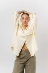 Sobrecamisa de gabardina liviana color crema, con corte oversize, cuello clásico, cierre frontal con botones a presión y dos bolsillos delanteros con solapa.