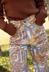 Pantalón tipo jean de corte recto con estampa exclusiva de diseño artístico en tonos tierra, ocres y azules. Presenta bolsillos traseros y cierre con botón metálico.