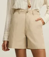 Bermuda de sastrería color beige, de cintura mediana y corte recto, confeccionada en sarga de algodón. Cuenta con trabillas para cinturón, cierre frontal tradicional y bolsillos laterales.