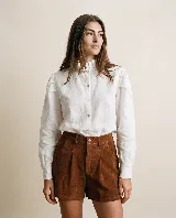 Camisa blanca de lino 100% natural, de manga larga con fruncidos en los hombros, cuello alto con volados y cierre frontal con botones.