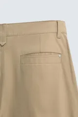 Pantalón chino de corte wide fit confeccionado en tejido de algodón. Presenta pliegues frontales, bolsillos laterales y bolsillos traseros de vivo, con cierre frontal de cremallera y botón.
