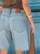 Bermuda de denim celeste de corte recto y largo hasta la rodilla, con tiro alto y etiqueta de cuero marrón con logo "azu" en la parte trasera de la cintura.