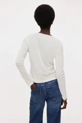 Saco entallado de punto suave, color blanco, con cuello redondo y cierre frontal de botones. Incorpora un panel interior cosido con efecto de top lencero con escote en V y ribete de encaje, creando un diseño de superposición.