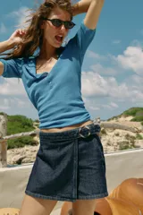 Falda pantalón cruzada de denim en color celeste, con diseño cruzado al frente, cierre frontal oculto y hebilla decorativa redonda en la cintura.