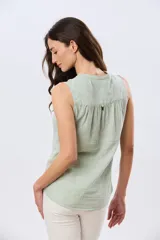 Musculosa de lino color beige, con cuello mao y escote en V, cierre frontal con botones y dos bolsillos plaqué con solapa en el pecho.