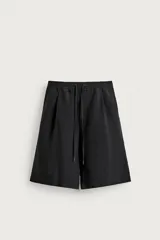 Bermuda relaxed fit de color negro, confeccionada en tejido fluido con viscosa y modal. Presenta cintura elástica ajustable con cordón, pliegues en el delantero, bolsillos frontales y bolsillos traseros de vivo.