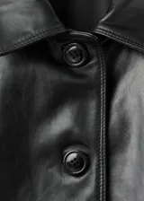 Chaqueta corta de cuero ovino color negro, con cuello camisero, cierre frontal con botones, mangas largas con puños elásticos y bolsillos laterales.