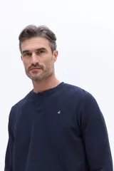 Remera tipo henley de manga larga en color azul marino, confeccionada en algodón con textura. Presenta una cartera con botones en el cuello y un pequeño logo bordado en el pecho.