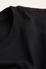 Remera de corte recto y suave tejido de algodón, color negro, con cuello redondo ribeteado y mangas cortas con hombros ligeramente caídos.