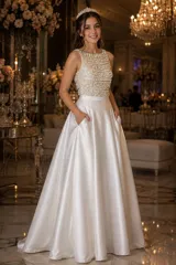 Vestido largo de fiesta color blanco, compuesto por un top sin mangas bordado con perlas y strass, y una falda amplia de piel de ángel con bolsillos y pretina alta.