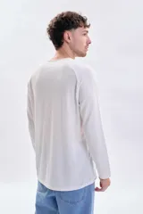 Remera manga larga de color blanco con cuello redondo a la base y mangas tipo raglán con textura acanalada.