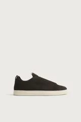 Zapatilla urbana de hombre confeccionada en piel con acabado de serraje, diseño minimalista sin cordones visibles y suela de goma a contraste.