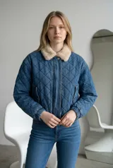 Campera de jean azul con diseño acolchado en forma de rombos, cuello de piel sintética en tono beige, cierre frontal con cremallera y puños elásticos.