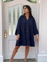 Vestido corto de lino color azul marino, con cuello mao, abotonadura frontal y volados en las mangas. Presenta un diseño amplio con frunces a la altura del busto y en la falda.