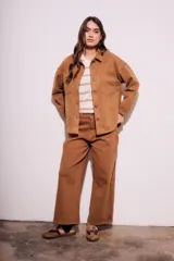 Sobrecamisa negra de estilo shacket, confeccionada en tejido de gamuza sintética. Presenta cuello camisero, cierre frontal de botones y dos bolsillos de parche con solapa en el pecho. El calce es oversize y las mangas son largas.