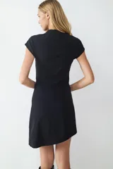 Vestido corto negro de manga corta con detalle cut out en el hombro, silueta recta y dobladillo asimétrico.