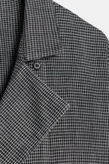 Camisa de corte oversize confeccionada en algodón, con estampado de cuadros pequeños en tonos grises. Presenta cuello solapa, cierre frontal con botones ocultos y mangas largas con puños rectos.