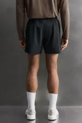 Pantalón corto deportivo color marrón oliva, confeccionado en tejido técnico ligero y elástico, con forro interior. Presenta cintura elástica ajustable con cordón, bolsillos frontales, bolsillo de seguridad trasero con cierre y aberturas laterales en el bajo.