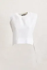 Remera crop top de lino color blanco, con cuello redondo y hombreras marcadas que le dan una estructura definida. Presenta un corte recto y holgado con aberturas laterales ajustables mediante cordones.