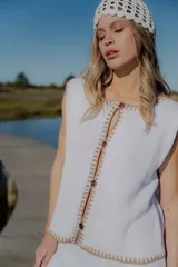 Conjunto de dos piezas tejido en algodón, compuesto por un chaleco sin mangas con cierre frontal de botones y un short de tiro medio. Ambas prendas presentan un diseño en color blanco con detalles de terminaciones en color beige.