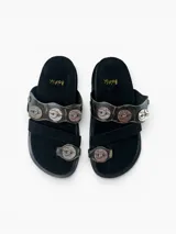 Sandalias planas de cuero negro con diseño de tiras anchas decoradas con apliques metálicos circulares grabados. Presentan una tira separadora para el dedo y plantilla forrada en cuero.