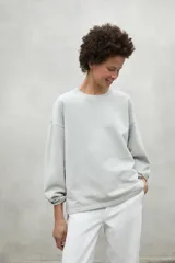 Buzo oversize color gris claro, con cuello redondo, hombros caídos y puños ajustados. Confeccionado con 50% algodón orgánico y 50% algodón reciclado.