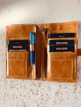 Portadocumentos de cuero color suela con cierre de cremallera y múltiples compartimentos para pasaportes, tarjetas y bolígrafo.