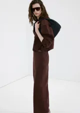 Pantalón marrón de corte recto y tiro medio, confeccionado en mezcla de lino, viscosa y algodón. Cuenta con diseño largo y cintura elástica.