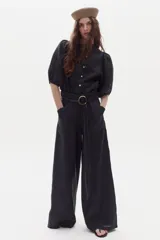 Pantalón negro de pierna ancha, tiro medio-alto, confeccionado en lino 100% natural, con bolsillos laterales y cierre frontal con gancho escondido.