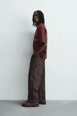 Camiseta de manga corta y cuello redondo, color granate oscuro, con estampado frontal en blanco que incluye texto y un escudo circular.