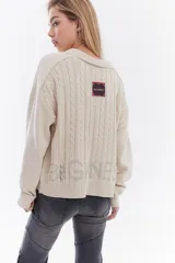 Cardigan de tejido de punto color marrón, con cuello solapa, cierre frontal de cremallera y diseño de trenzas. Cuenta con puños y dobladillo en rib elástico y un pequeño bordado en el pecho.